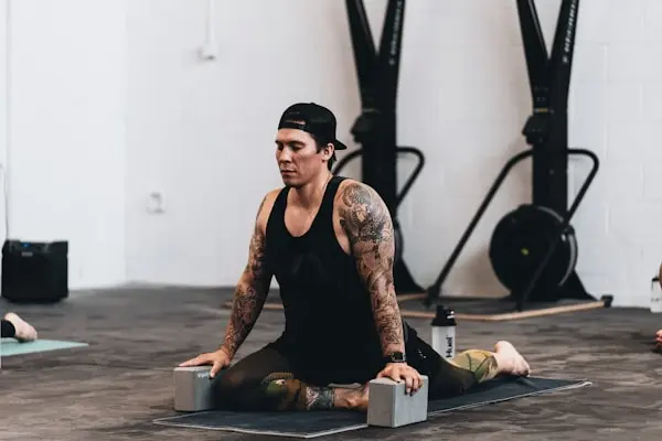 Person performing a seated stretch on a yoga mat using yoga blocks in a gym studio