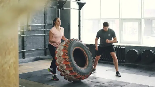 Two people performing a functional training exercise using a large tyre in a gym