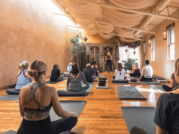 Group fitness class seated on yoga mats in a calm studio while an instructor leads the session