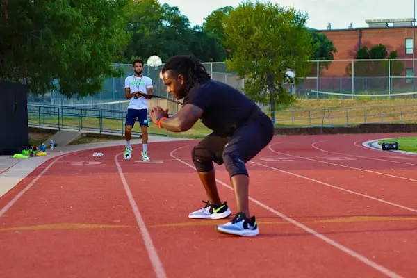 Person performing a squat exercise on an outdoor running track while a coach observes