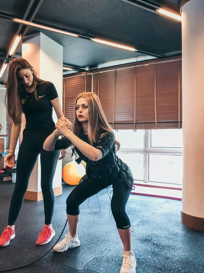 Personal trainer guiding a client through a squat exercise using resistance equipment in a gym
